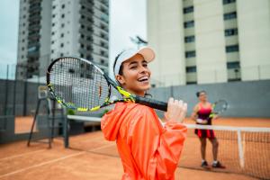 A smiling woman holding a tennis racquet representing tennis elbow prevention in spring sports activities.