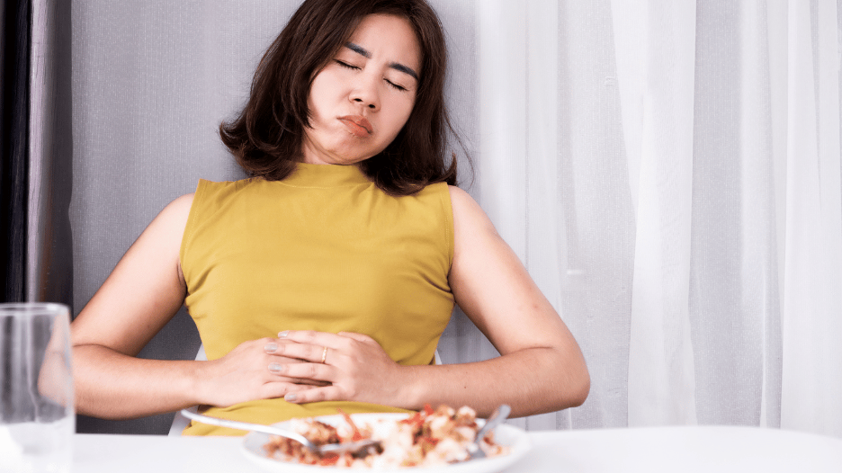 Woman in yellow top holding stomach showing discomfort from bloating after eating a meal