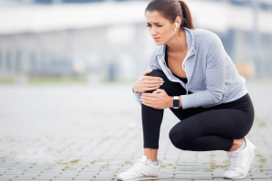 Woman experiencing leg cramp pain while exercising outdoors, holding her knee