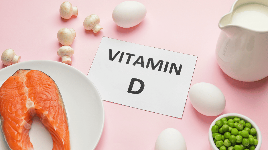 Vitamin D rich foods, including salmon, eggs, mushrooms, and milk, on a pink background