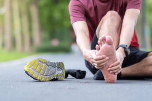 Person holding heel with visible pain, a common symptom of plantar fasciitis that can last weeks or months without treatment